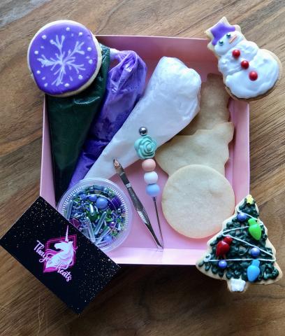 three decorated cookies around a box of decorating supplies and a business card for Thayer Treats