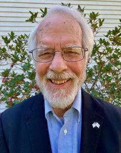 William Hall a white man with facial hair and glasses wearing a suit standing outside