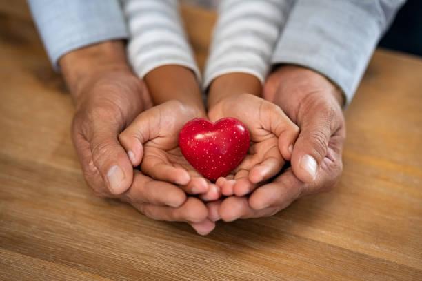 two pairs of hands holding a red heart